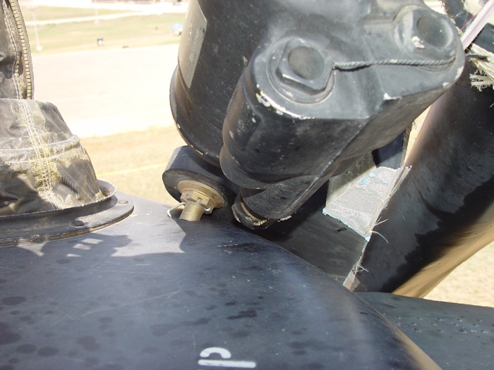 July 2002: This photograph shows extensive damage to the aft rotor system. A lead-lag dampner has broken off allowing the green blade to strike the fuselage and ground. A mount bolt from the dampner has punctured a hole in the rainshield.