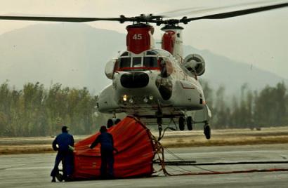 Airframe and power plant mechanics, foreground, hold a Bambi basket, which can hold 2,000 gallons of water, steady as a Boeing 234 Chinook takes off to fight wild fires in the San Bernardino mountains on Thursday, 30 October 2003, at San Bernardino Helibase in San Bernardino, California. Thirty-five airtankers and 86 helicopters have been attacking the flames from all Southern California wild fires since October 21st.
