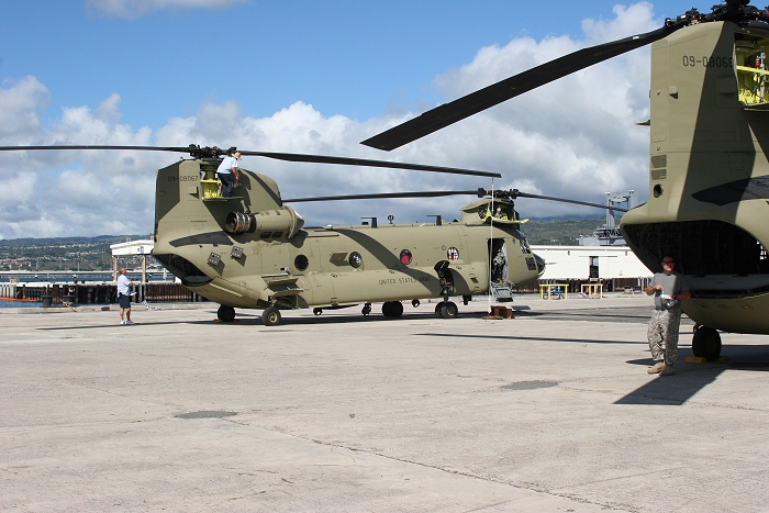 20 November 2010: As CW4 Jack Tartaglia seeks refuge from the sun under 09-08068, CH-47F Chinook helicopter 09-08067 gets some final maintenance during reassembly on the dock at Pearl Harbor.
