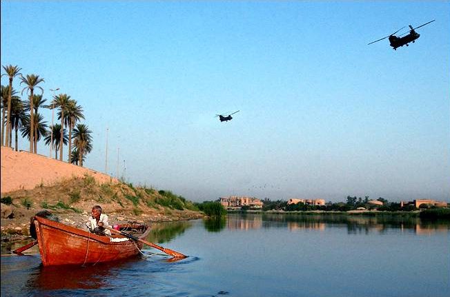 Two U.S. Army CH-47D Chinook helicopters pass an Iraqi fisherman as he works the Tigris River.