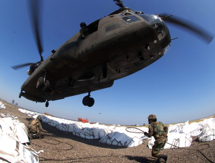 9 September 2005: Army National Guardsmen Specialist Clint Aucoia and Private First Class Christopher Tiffit attach cargo hooks supporting large sandbags to a CH-47 Chinook helicopter. The sandbags are being used to plug a New Orleans levee which was breached during Hurricane Katrina.